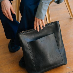 Woman sitting with black leather convertible backpack, handmade full grain vegetable tanned leather bag