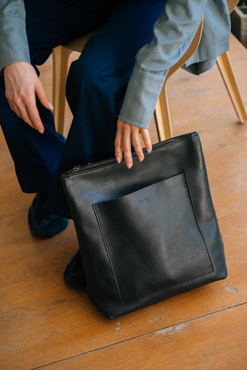 Woman sitting with black leather convertible backpack, handmade full grain vegetable tanned leather bag