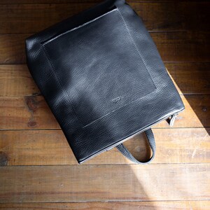 Black full grain leather convertible backpack front view on wooden surface, handmade rucksack