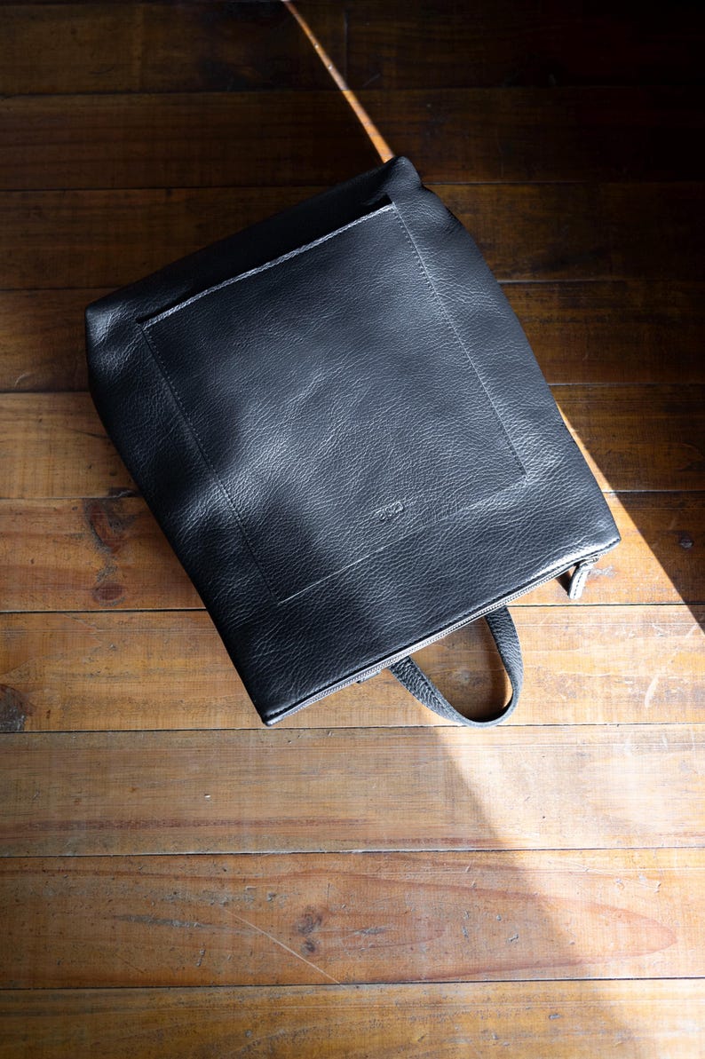Black full grain leather convertible backpack front view on wooden surface, handmade rucksack