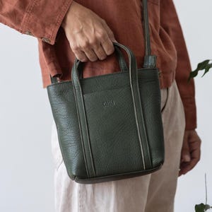 Woman carrying forest green leather bag by top handle in casual setting