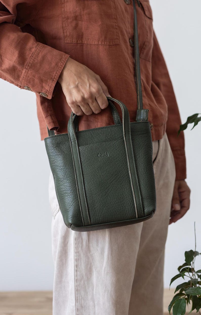 Woman carrying forest green leather bag by top handle in casual setting