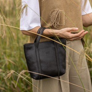 Woman carrying black leather bag in outdoor city setting