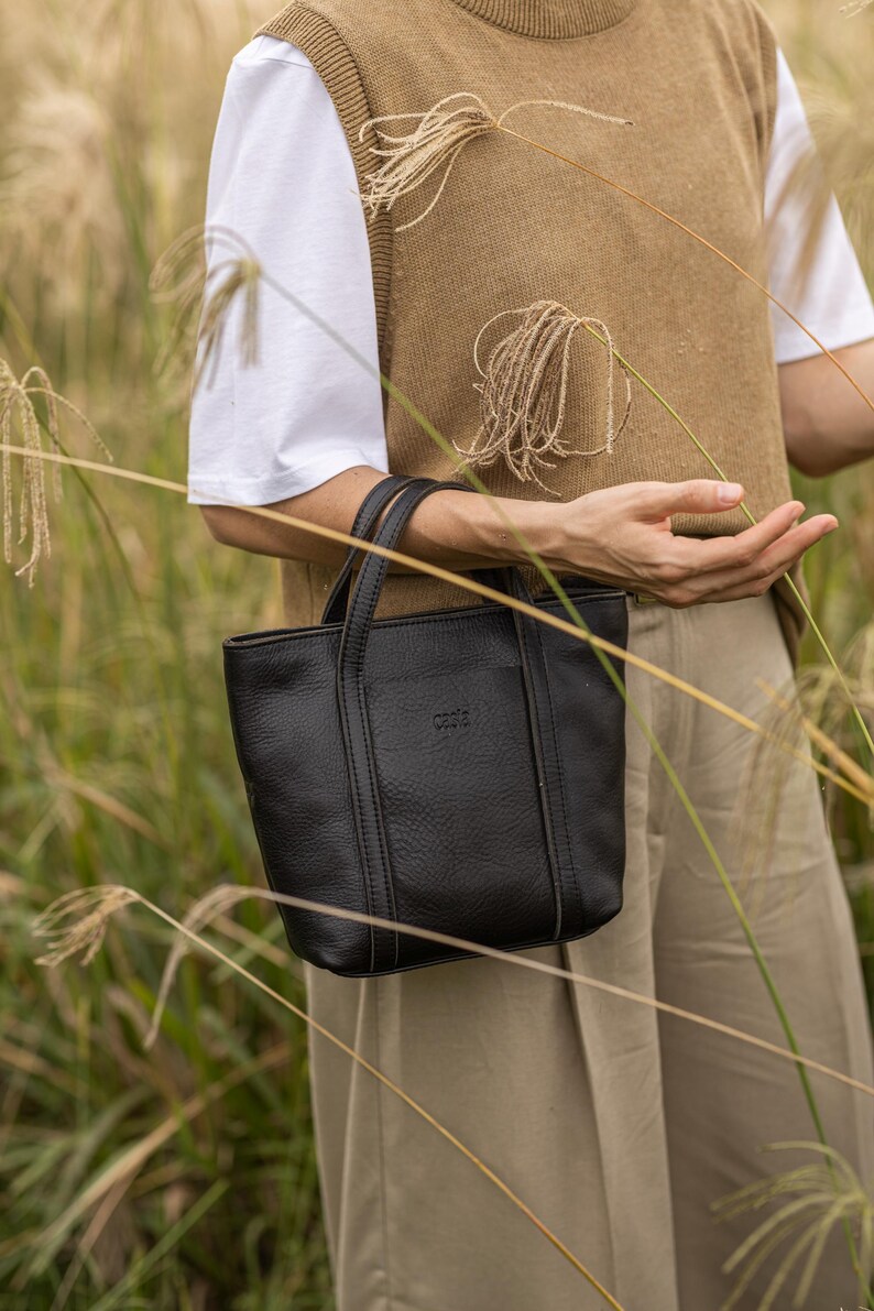 Woman carrying black leather bag in outdoor city setting