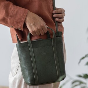 Hands holding open olive green leather bag showing capacity and top handle
