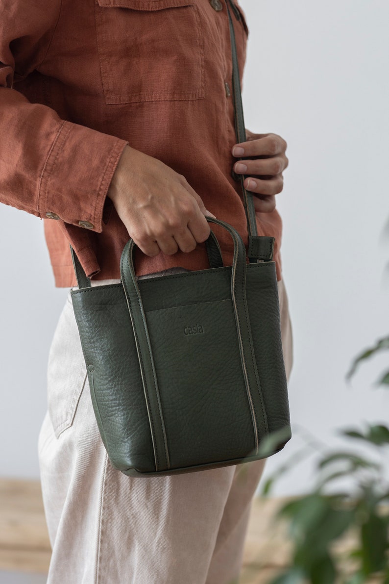 Hands holding open olive green leather bag showing capacity and top handle
