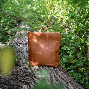 Caramel leather convertible backpack in garden setting, full grain vegetable tanned handmade leather bag