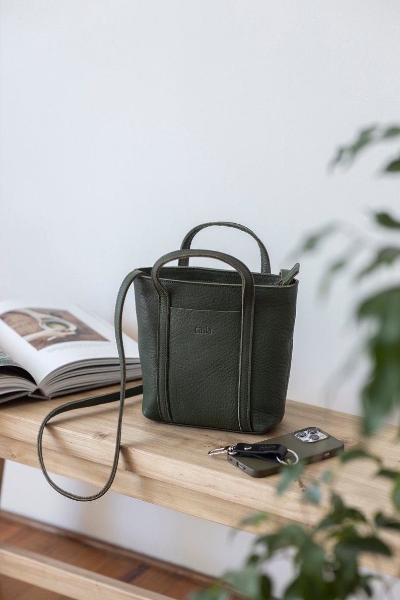 Forest green full grain leather crossbody bag with adjustable strap on desk