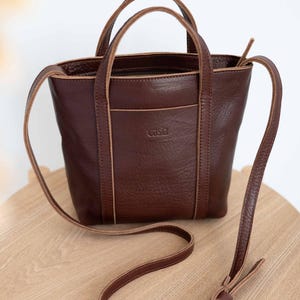 Bordeaux full grain leather bag with long crossbody strap on wooden surface