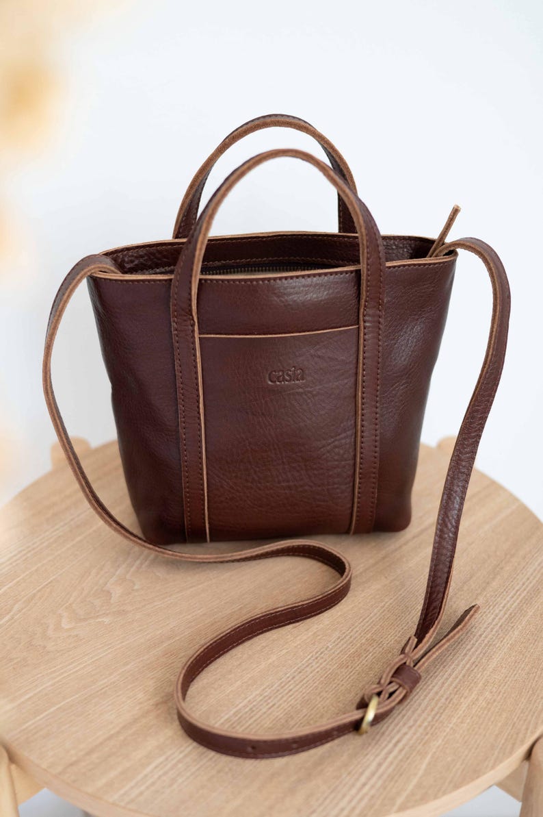 Bordeaux full grain leather bag with long crossbody strap on wooden surface