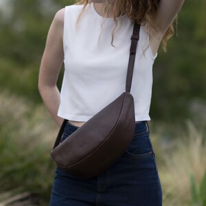 Woman in jeans wearing chocolate full grain leather banana bag crossbody, handmade vegetable tanned moon shape belt bag everyday urban lifestyle
