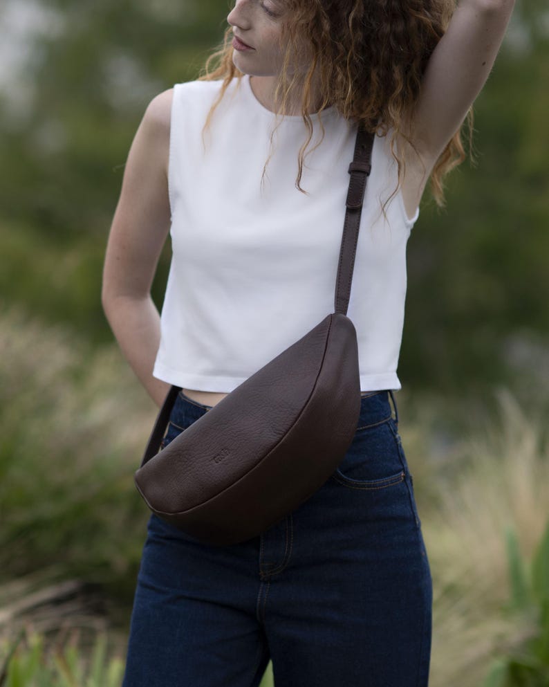 Woman in jeans wearing chocolate full grain leather banana bag crossbody, handmade vegetable tanned moon shape belt bag everyday urban lifestyle