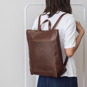 Woman from behind wearing brown leather convertible backpack, handmade full grain vegetable tanned rucksack