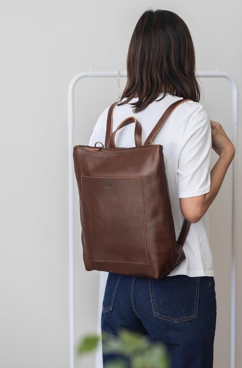 Woman from behind wearing brown leather convertible backpack, handmade full grain vegetable tanned rucksack