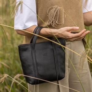 Woman in olive vest carrying black leather crossbody bag outdoors