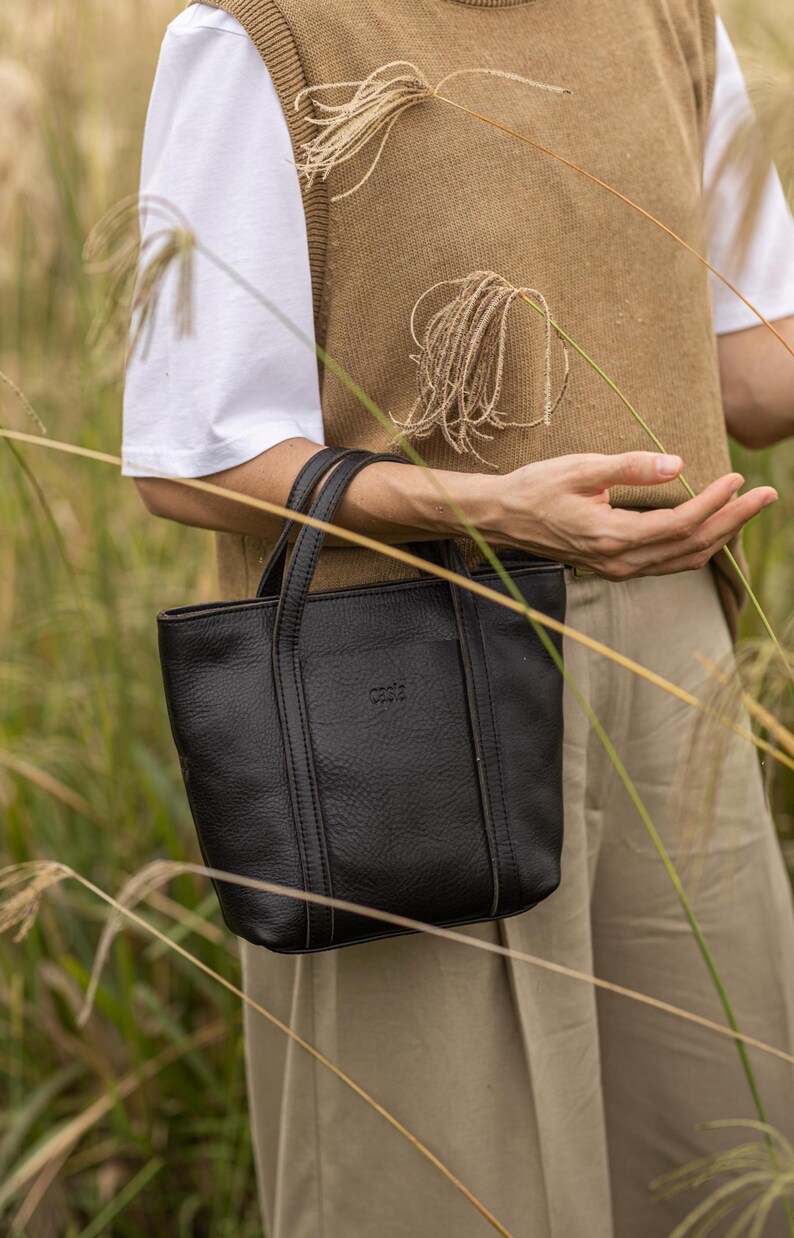 Woman in olive vest carrying black leather crossbody bag outdoors