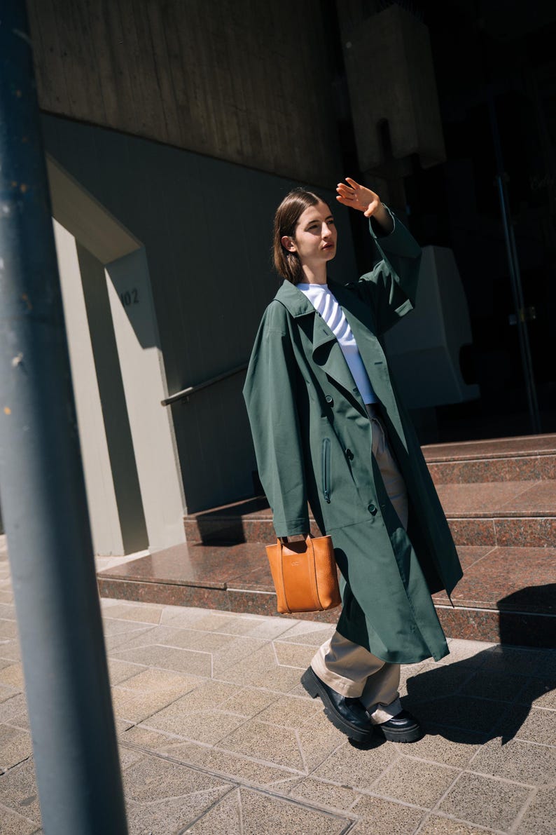 Woman in long green coat carrying camel leather crossbody bag in urban setting
