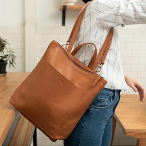 Woman from behind wearing caramel leather convertible backpack in interior setting, handmade full grain leather diaper bag