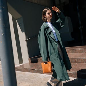Woman in long green coat carrying camel leather crossbody bag in urban setting