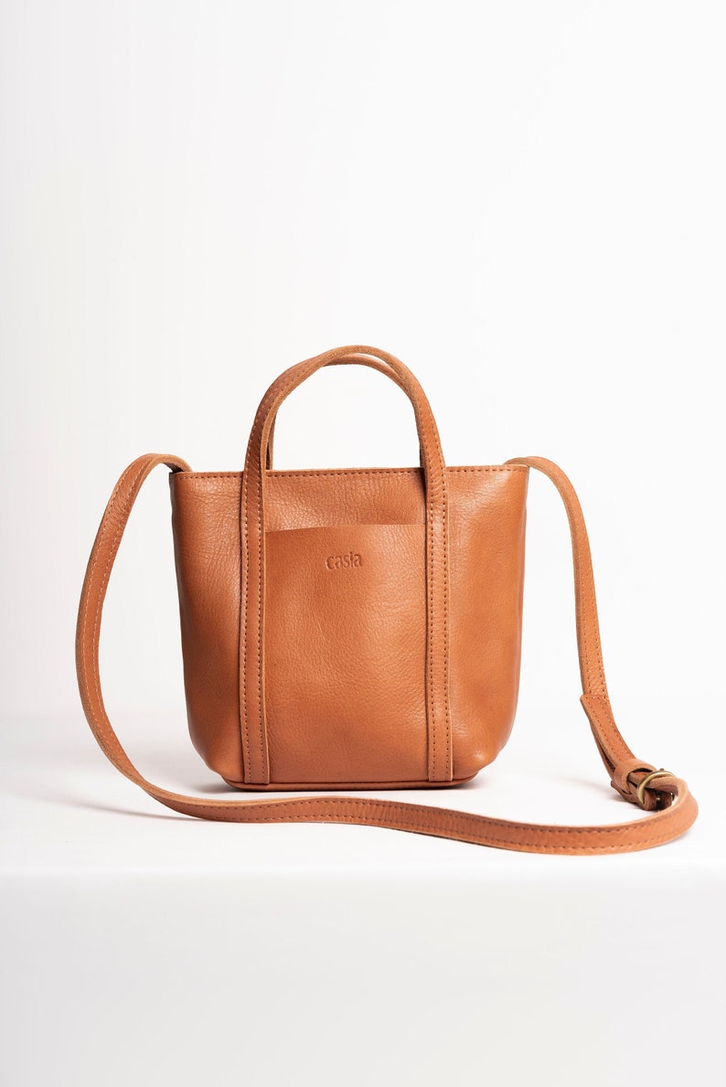 Tan full grain leather crossbody bag with adjustable strap on white background