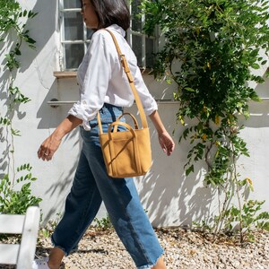 Woman walking with mustard leather crossbody bag in outdoor city setting