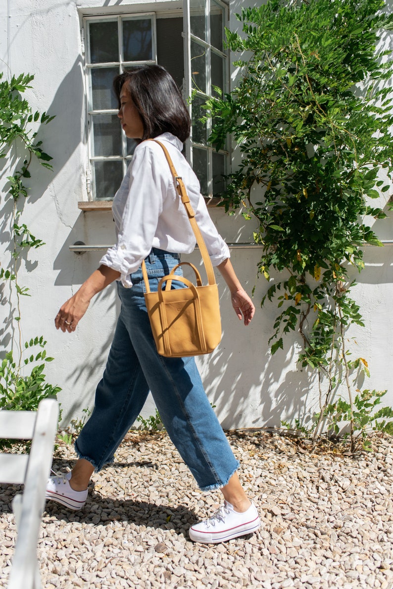 Woman walking with mustard leather crossbody bag in outdoor city setting
