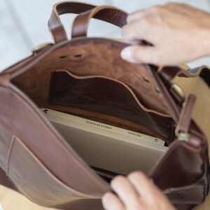 Hands opening brown leather convertible backpack showing unlined interior, full grain vegetable tanned leather