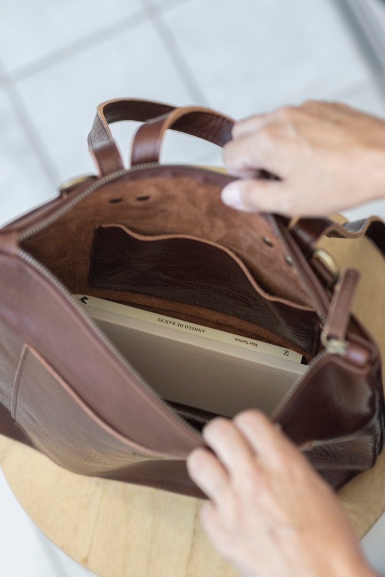Hands opening brown leather convertible backpack showing unlined interior, full grain vegetable tanned leather
