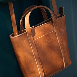 Brown leather tote bag with top handle against dark teal background