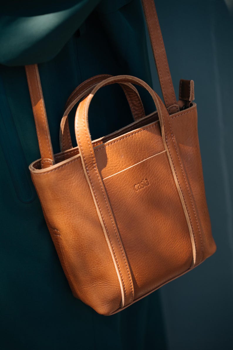 Brown leather tote bag with top handle against dark teal background