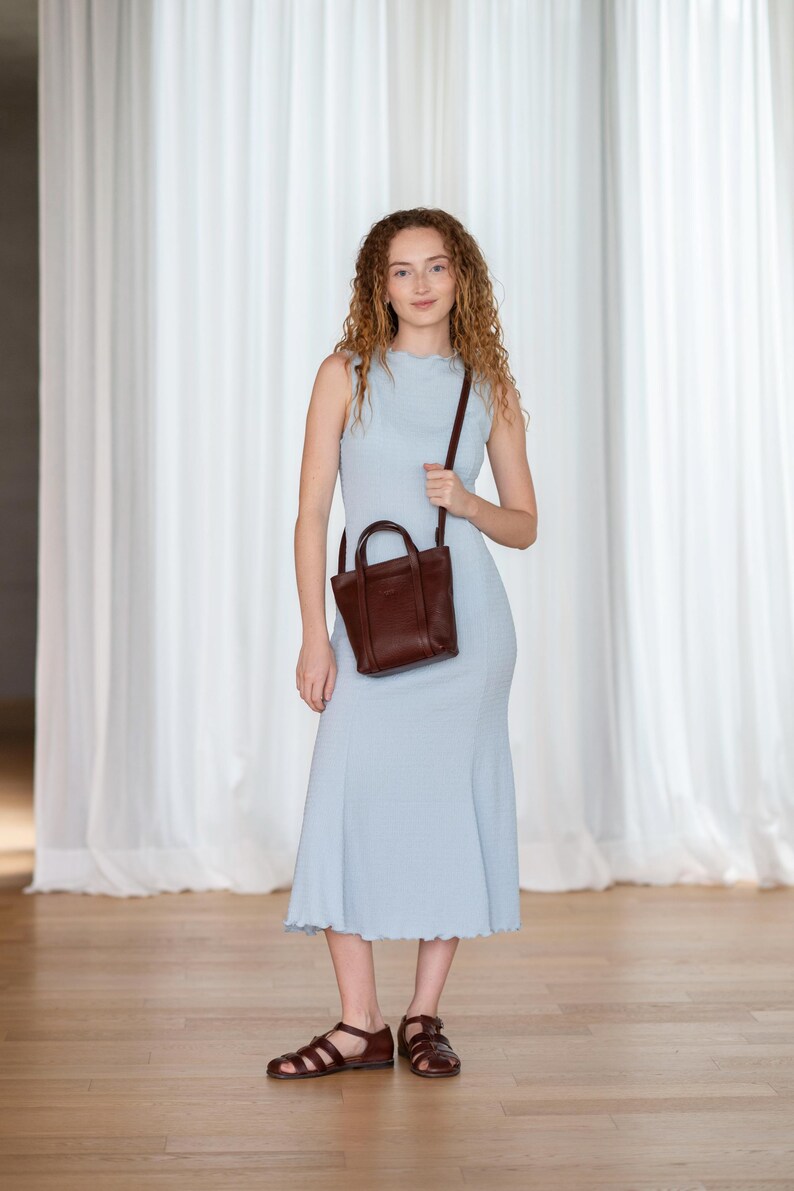 Young woman carrying bordeaux leather bag by top handle with blue dress