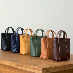 Six color options of handmade leather tote bag displayed on wooden surface