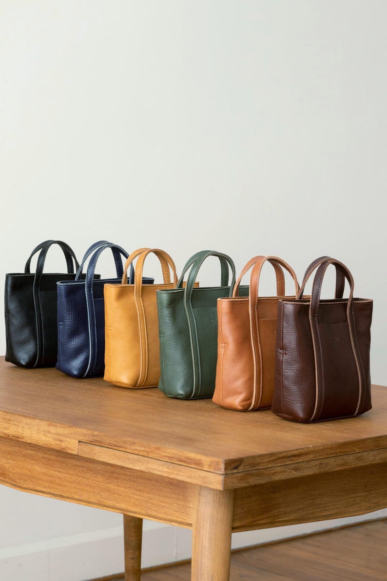 Six color options of handmade leather tote bag displayed on wooden surface