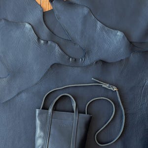 Navy leather crossbody bag with top handle on leather background
