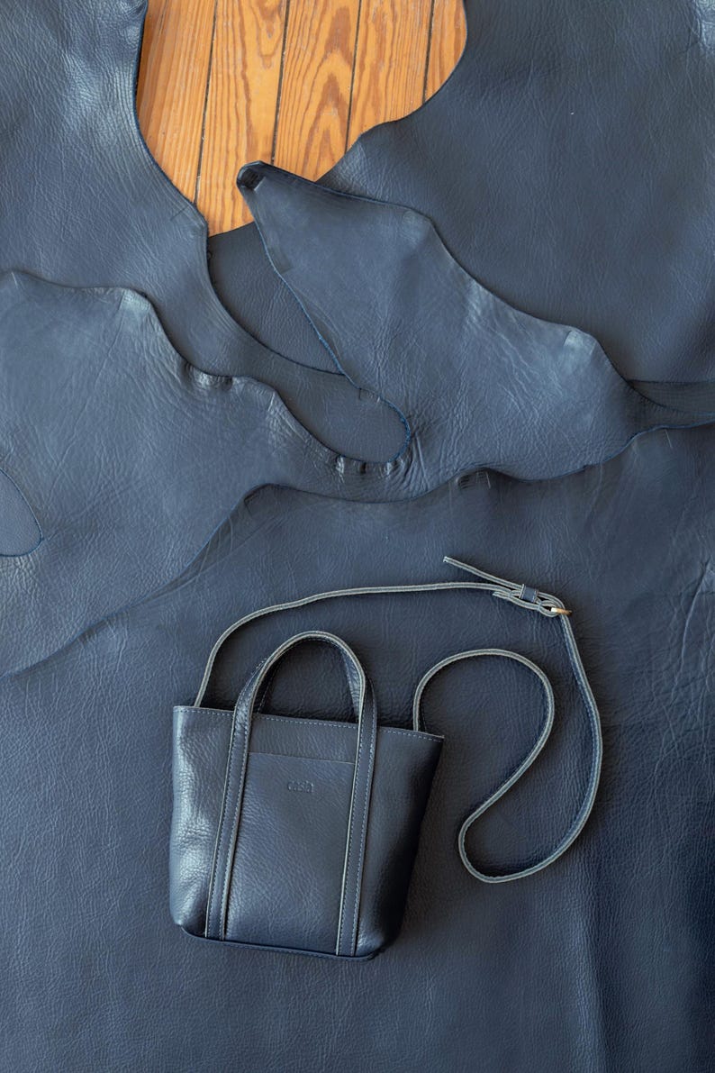 Navy leather crossbody bag with top handle on leather background