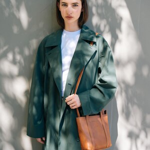 Model wearing tan leather crossbody bag with green coat in natural light