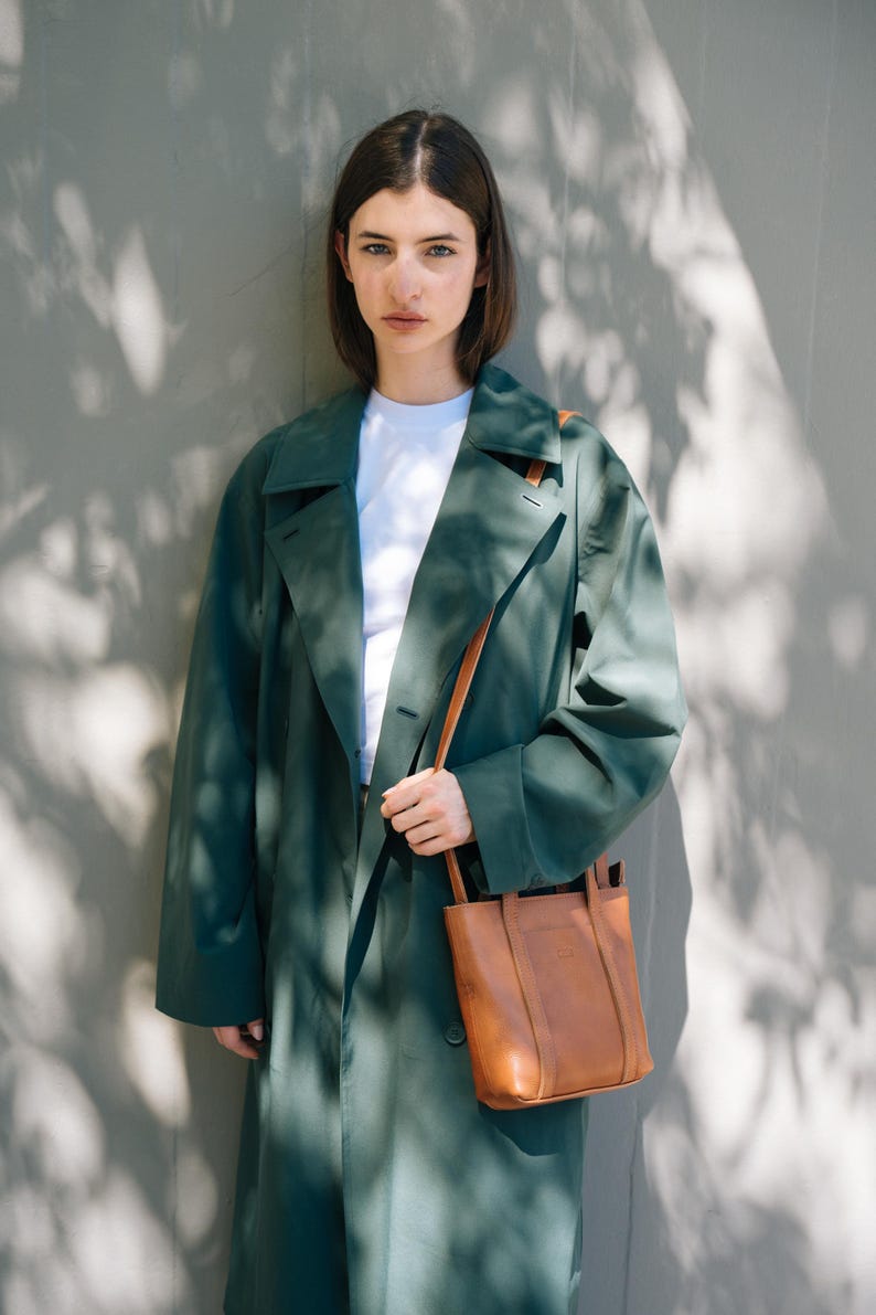 Model wearing tan leather crossbody bag with green coat in natural light
