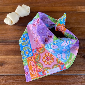 May include: A colorful paisley bandana with a pink, blue, green, and orange pattern. The bandana has a small yellow tag with the text "mostly sunny" on it.