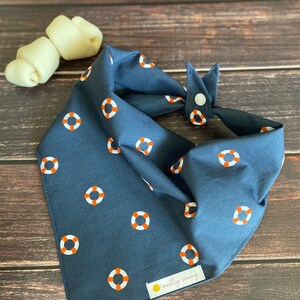 May include: A navy blue bandana with a white and orange life preserver pattern. The bandana has a snap closure and a small label that says "mostly sunny".