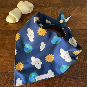 May include: A blue bandana with a white background featuring a repeating pattern of suns, clouds, and globes. The bandana has a small tag that reads "mostly sunny".