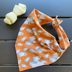 May include: Orange bandana with a white ghost pattern and the text "mostly sunny" on the bottom right corner.