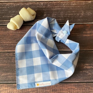 May include: A blue and white gingham dog bandana with a light blue button and a label that says "mostly sunny".