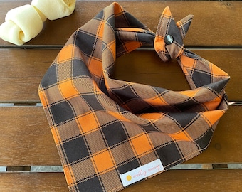 May include: Orange and black plaid bandana with a "mostly sunny" label. The bandana is tied in a knot and is on a wooden surface.