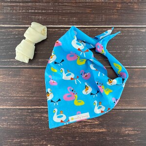 May include: A blue bandana with a white swan and pink flamingo pool float pattern. The bandana has the text "motley crew" in a yellow circle.