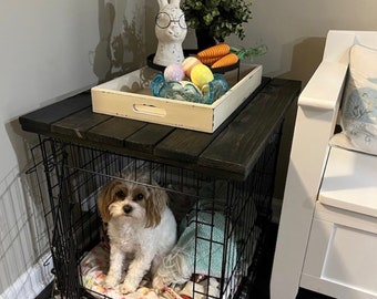 Può includere: Un piano in legno nero con un vassoio bianco sopra. Il vassoio contiene una statuetta di coniglio bianco, uova di Pasqua colorate e carote. Il tavolo è sopra una gabbia per cani in metallo nero con un cane bianco dentro.