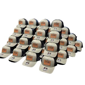May include: A stack of 24 gray and black trucker hats with a brown leather patch that says "CAM" on each hat.