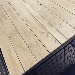 May include: Weathered oak wood tabletop with a light brown color and a natural wood grain pattern. The wood is arranged in horizontal planks.