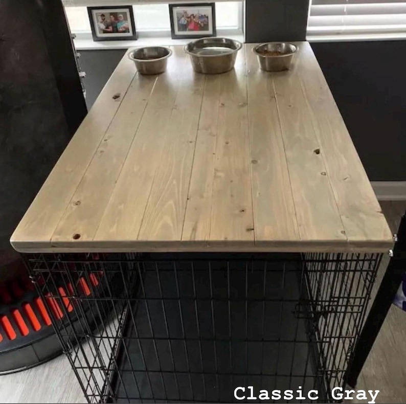 May include: A rectangular wooden table top with a light gray finish, featuring visible wood grain and knots. Three stainless steel bowls are placed in a row on the surface. The table is supported by a black metal wire crate base. Classic Gray.
