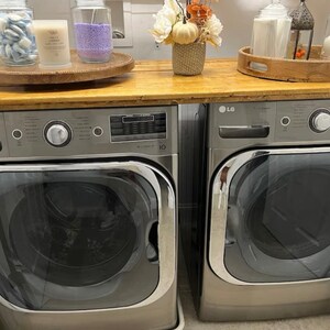 May include: Two stainless steel washing machines side-by-side. The washing machine on the left has a digital display and a control knob. The washing machine on the right has a digital display and a control knob. Both washing machines have a silver finish.