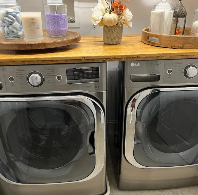 May include: Two stainless steel washing machines side-by-side. The washing machine on the left has a digital display and a control knob. The washing machine on the right has a digital display and a control knob. Both washing machines have a silver finish.